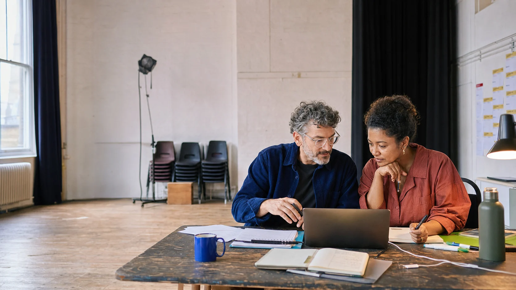 Two arts administrators working together at a laptop in a rehearsal room